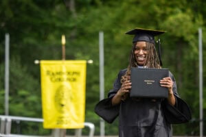 A graduate in a cap and gown smiles with her diploma after exiting the stage 