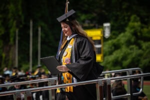 A graduate in a cap and gown smiles with her diploma after exiting the stage 