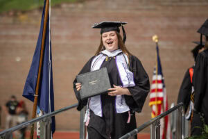 Stephanie Swithers '25 smiles as she holds her diploma onstage