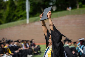 Sonia Langhorne '25 holds her diploma high in the air as she walks off the stage at Commencement 