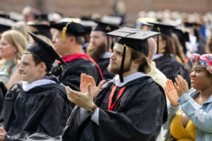A student in his cap and gown claps during Commencement 