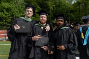 Three male students pose for a photo together after Commencement, holding their diplomas 