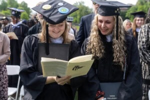 Two students in the crowd look at the commencement program, smiling 