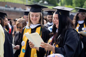 Two students in the crowd look at the commencement program, smiling 