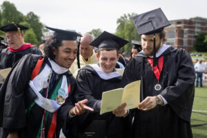 Students in the crowd look at the commencement program, smiling 