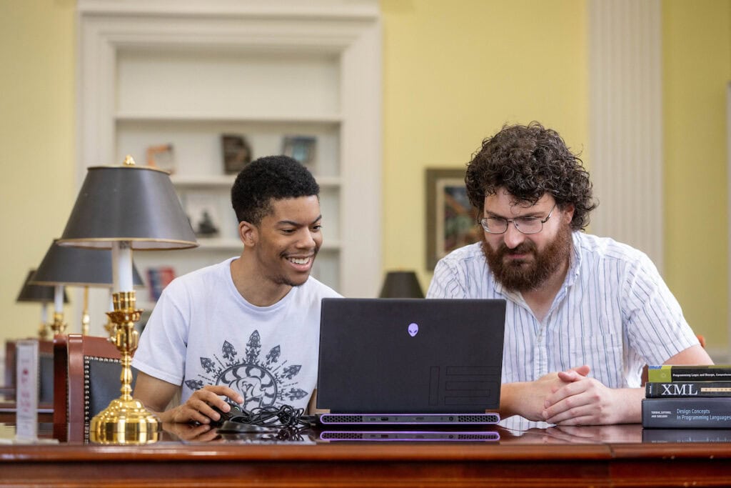 A student and a professor sit together, both looking at a laptop. A student and a professor sit together, both looking at a laptop.