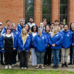 A group photo with everyone wearing matching blue jackets for a program