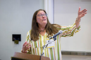 A woman with glasses and a striped shirt is giving a speech.