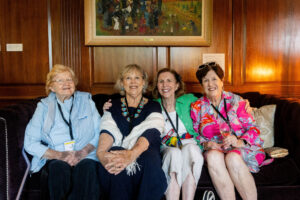 A group of alums pose for a photo together, sitting down on a couch 