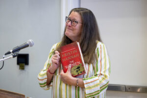 A woman with glasses and a striped shirt is giving a speech.