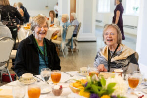 Two women sitting at a table with food and drinks.