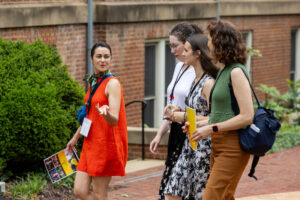 Three women walking on a brick walkway with a man holding a book.
