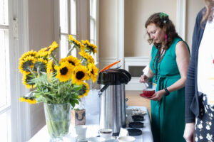 A woman gets some coffee from a table where a big bouquet of sunflowers sits in a vase 