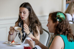 Two women sitting at a table with food and drinks.