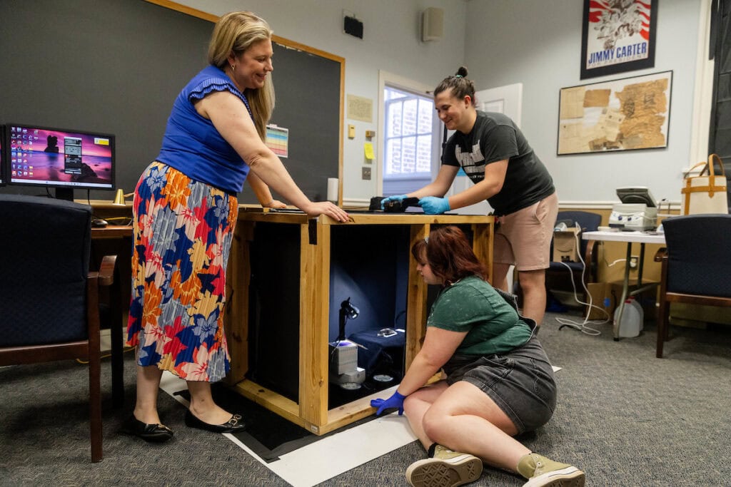 Three people working on a piece of equipment in a classroom