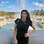 A woman in a black dress standing next to a fountain.
