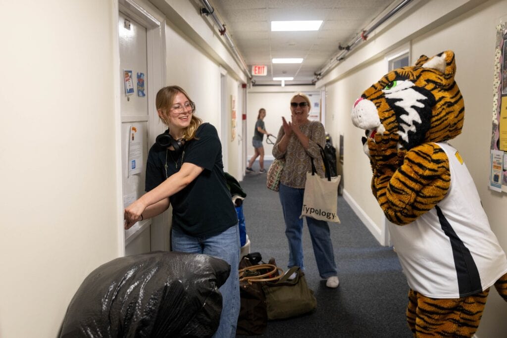 A woman is standing in a hallway with a tiger mascot.
