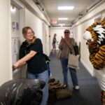 A woman is standing in a hallway with a tiger mascot.