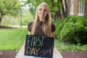 A student holds a chalkbaord that says "First Day Slay" 