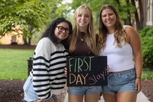 Three students pose with a chalkboard that says "First Day Slay" 