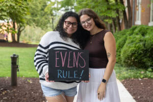 Two students pose with a chalkboard that says "Evens Rule"
