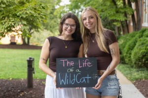Two students pose with a chalkboard that says "The Life of a WildCat"