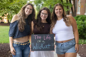 Three students pose with a chalkboard that says "The Life of a WildCat"