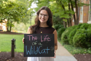 A student poses with a chalkboard that says "The Life of a WildCat"