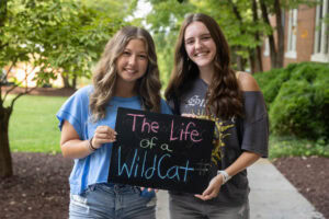 Two students pose with a chalkboard that says "The Life of a WildCat"