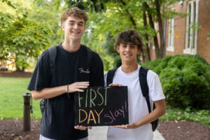 Two students pose with a chalkboard that says "First Day Slay"