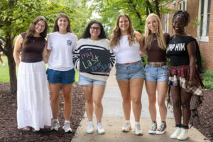 A group of students pose together holding chalkboards with funny sayings on them