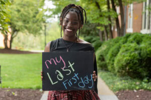 A student poses with a chalkboard that says "My Last First Day" 