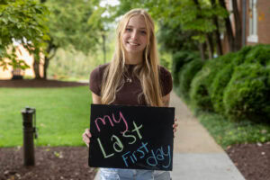 A student poses with a chalkboard that says "My Last First Day" 