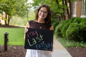 A student poses with a chalkboard that says "My Last First Day" 