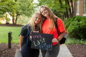 Two students pose with a chalkboard that says "My Last First Day" 