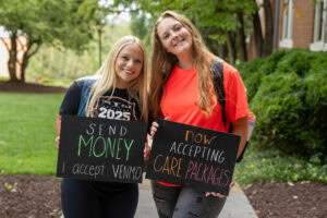Two students pose together holding chalkboards with funny sayings on them