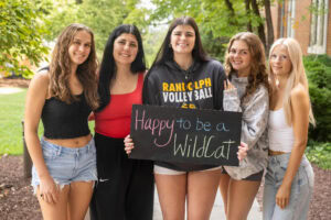A group of students pose together holding chalkboards with funny sayings on them