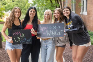 A group of students pose together holding chalkboards with funny sayings on them