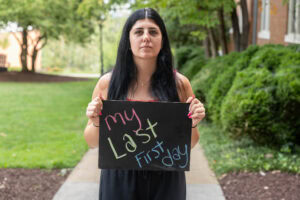 A student poses with a chalkboard that says "My Last First Day" 