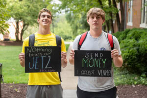 Two students pose together holding chalkboards with funny sayings on them