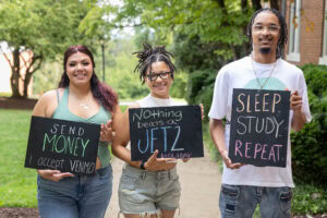 A group of students pose together holding chalkboards with funny sayings on them