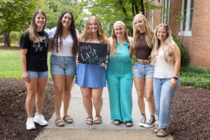 A group of students pose together holding chalkboards with funny sayings on them