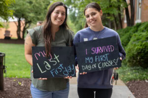 Two students pose together holding chalkboards with funny sayings on them