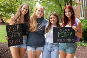 A group of students pose together holding chalkboards with funny sayings on them