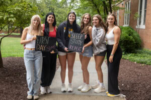 A group of students pose together holding chalkboards with funny sayings on them