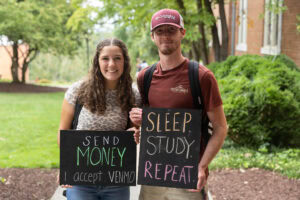 Two students pose together holding chalkboards with funny sayings on them