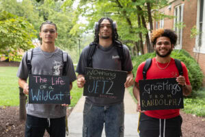 A group of students pose together holding chalkboards with funny sayings on them