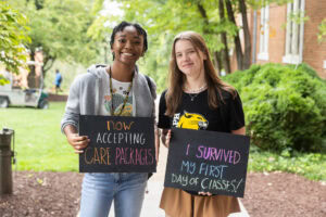 Two students pose together holding chalkboards with funny sayings on them