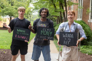 A group of students pose together holding chalkboards with funny sayings on them