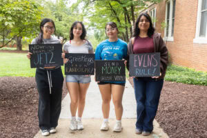 A group of students pose together holding chalkboards with funny sayings on them